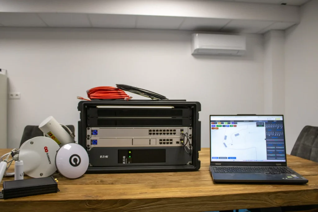 Drone control equipment and networking hardware on a table, with a laptop displaying a drone show interface.