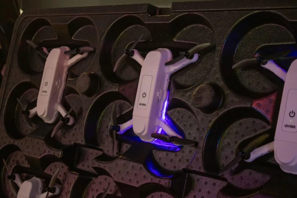 Close-up of several small white drones stored in a protective case, with one drone illuminated by a purple light.
