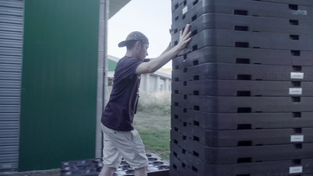 A Drotek team member stacking drone landing pad trays outdoors near storage buildings during light show equipment setup.