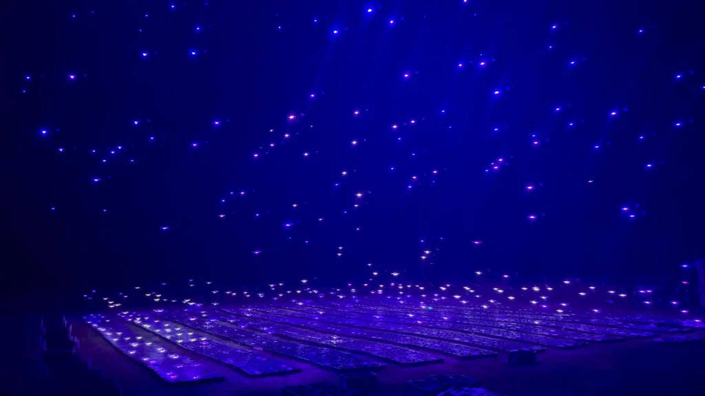 Rows of drones lighting up and taking off from a launch field into a deep blue night sky during a drone light show